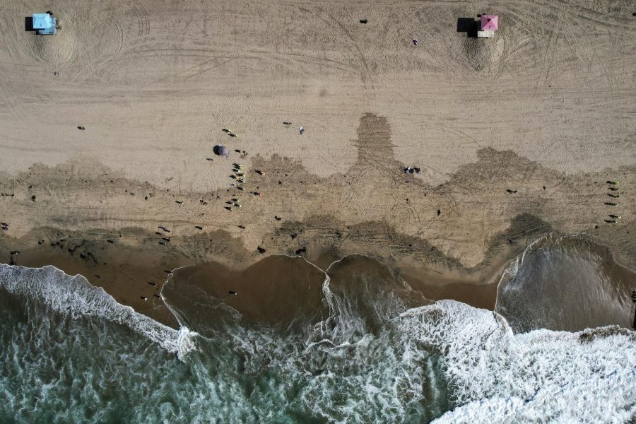  This Monday, Oct. 11, 2021, aerial file photo taken with a drone, shows beachgoers as workers in protective suits continue to clean the contaminated beach in Huntington Beach, Calif. 
