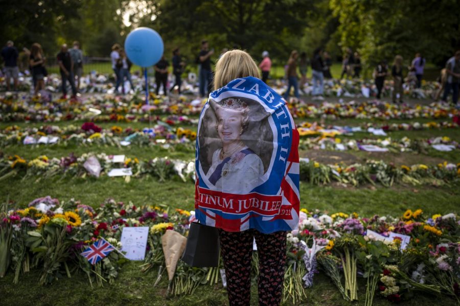 A woman carrying a flag with Queen Elizabeth's image stands at Green Park memorial, next to Buckingham Palace in London, Sunday, Sept. 11, 2022.