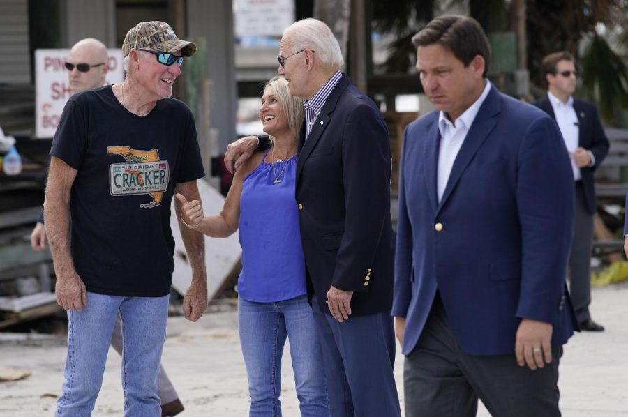President Joe Biden talks with people impacted by Hurricane Ian as he tours the area impacted by Hurricane Ian on Wednesday, Oct. 5, 2022, in Fort Myers Beach, Fla. Florida Gov. Ron DeSantis walks by at right.